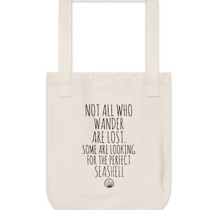 May include: A white canvas tote bag with black text that reads "Not all who wander are lost. Some are looking for the perfect seashell."  A small seashell graphic is below the text.