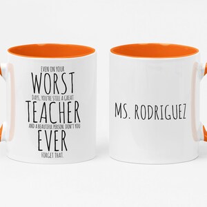 May include: White ceramic mug with an orange interior and handle. The mug features the text "EVEN ON YOUR WORST DAYS, YOU'RE STILL A GREAT TEACHER" on one side and "MS. RODRIGUEZ" on the other. A thoughtful gift for a teacher.