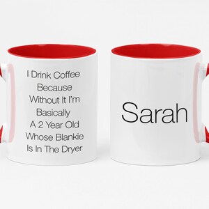 May include: White ceramic coffee mug with a red rim and handle. The mug has black text that reads "I Drink Coffee Because Without It I'm Basically A 2 Year Old Whose Blankie Is In The Dryer". The other side of the mug has the name "Sarah" in black text.