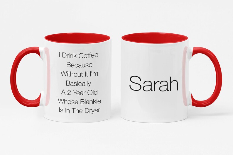 May include: White ceramic coffee mug with a red rim and handle. The mug has black text that reads "I Drink Coffee Because Without It I'm Basically A 2 Year Old Whose Blankie Is In The Dryer". The other side of the mug has the name "Sarah" in black text.