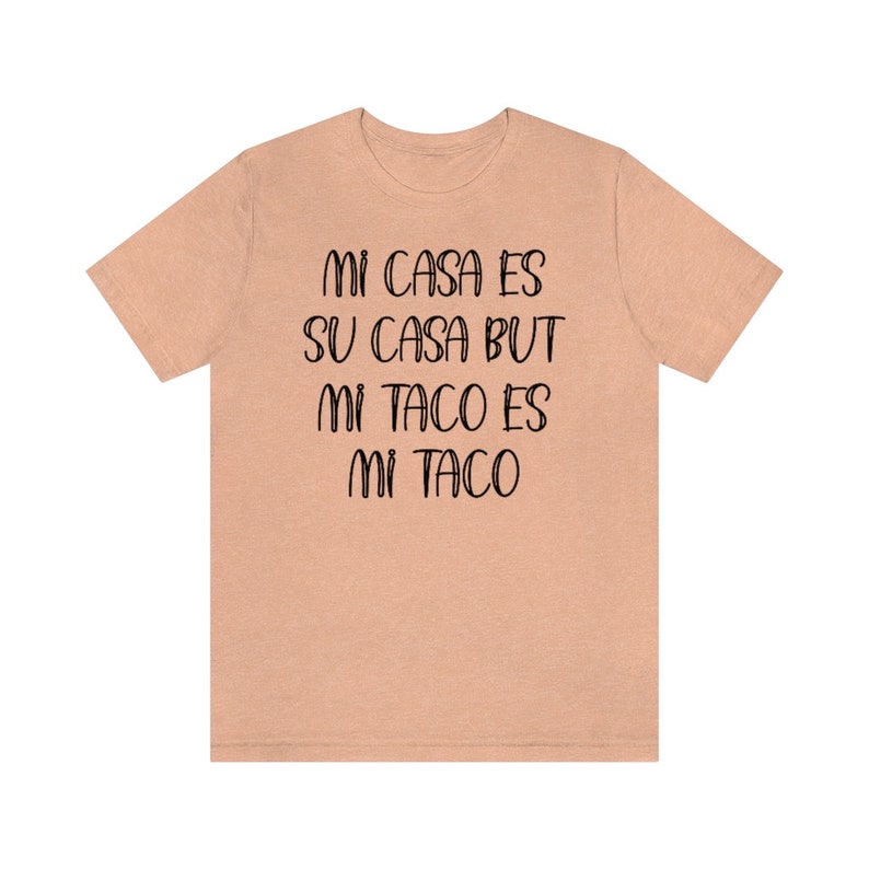 Puede incluir: Una camiseta de color melocot&oacute;n con el texto "Mi casa es su casa but mi taco es mi taco" impreso en negro.