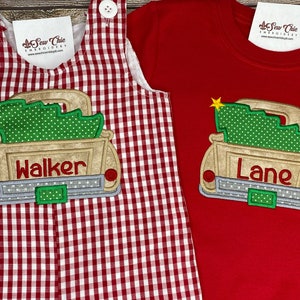 May include: Two Christmas-themed outfits for boys. One outfit is a red and white gingham overall with a white truck carrying a Christmas tree and the name "Walker" embroidered on the back. The other outfit is a red long-sleeve shirt with a white truck carrying a Christmas tree and the name "Lane" embroidered on the back.
