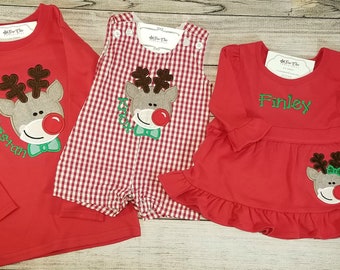 May include: Red, white, and green Christmas outfits for children. The outfits feature a reindeer design with a red nose and green bow tie. The outfits are personalized with the names "Tristan", "Kiah", and "Finley".