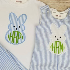 May include: A blue and white striped baby outfit with a white bunny applique and green monogram. The bunny has a green circle with the monogram "HRN" inside.