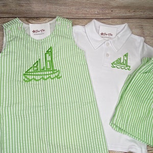 May include: A green and white striped outfit for a baby or toddler. The outfit includes a sleeveless romper, a short-sleeved polo shirt, and shorts. The romper and shorts have a sailboat design with the initials "BLG" embroidered on them. The polo shirt has the same sailboat design embroidered on the front.