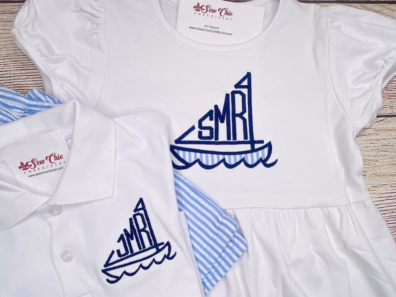 May include: White embroidered polo shirt and dress with blue sailboat design and the initials "SMR" on the sail. The dress has a blue and white striped trim.