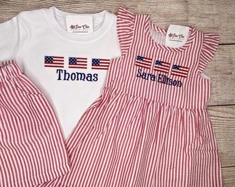 May include: A red and white striped dress and matching shorts set for children. The dress has a ruffled neckline and the shorts have a simple design. Both pieces feature embroidered American flags and personalized names, "Sara Ellison" and "Thomas".