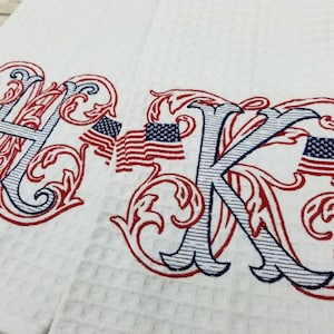 May include: Two white kitchen towels with red and blue embroidered letters "HK" surrounded by red and blue floral designs and American flag motifs.
