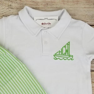 May include: White polo shirt with a green embroidered sailboat design featuring the initials "HCW".