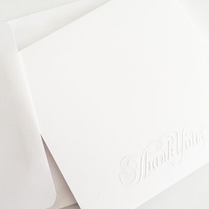 May include: A white card with a raised, embossed script that reads "Thank You".