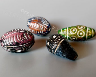 May include: Four colorful ceramic beads with intricate designs. The beads are oval shaped and have a glossy finish. The beads are in shades of green, blue, red, and black.