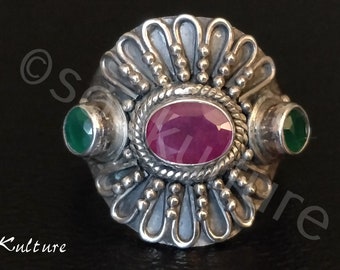 Op de afbeelding: Een zilveren ring met een roze ovale edelsteen omringd door twee groene ronde edelstenen. De ring heeft een decoratief ontwerp met een bloemmotief.