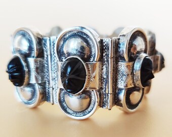 May include: A silver bracelet with three black onyx stones. The bracelet is made of interlocking links and has a decorative design.