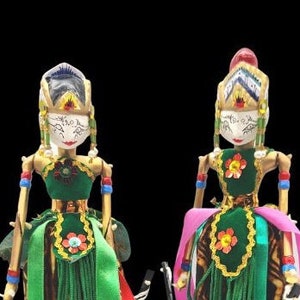 May include: Two traditional Indonesian shadow puppets, or wayang kulit, with colorful costumes and intricate details. The puppets are on stands with blue bases and the text "Shinta" and "Rama" on the bases.