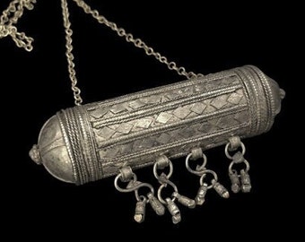 May include: A silver-toned pendant necklace with a cylindrical body and decorative patterns. The pendant hangs from a delicate chain and features small dangling charms. The design suggests an antique or vintage aesthetic.