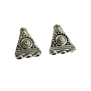 May include: Two silver triangle-shaped bead caps with intricate designs and three small round beads on the bottom.