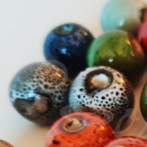May include: A collection of colorful ceramic beads with various patterns and textures. The beads are round and have a glossy finish. Some of the beads have a speckled or marbled appearance.