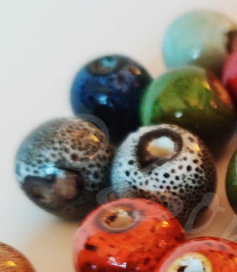 May include: A collection of colorful ceramic beads with various patterns and textures. The beads are round and have a glossy finish. Some of the beads have a speckled or marbled appearance.