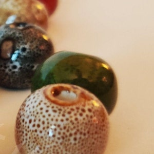 May include: A close-up of a collection of ceramic beads. The beads are various colors and have a speckled texture. The beads are round and have a hole in the center.