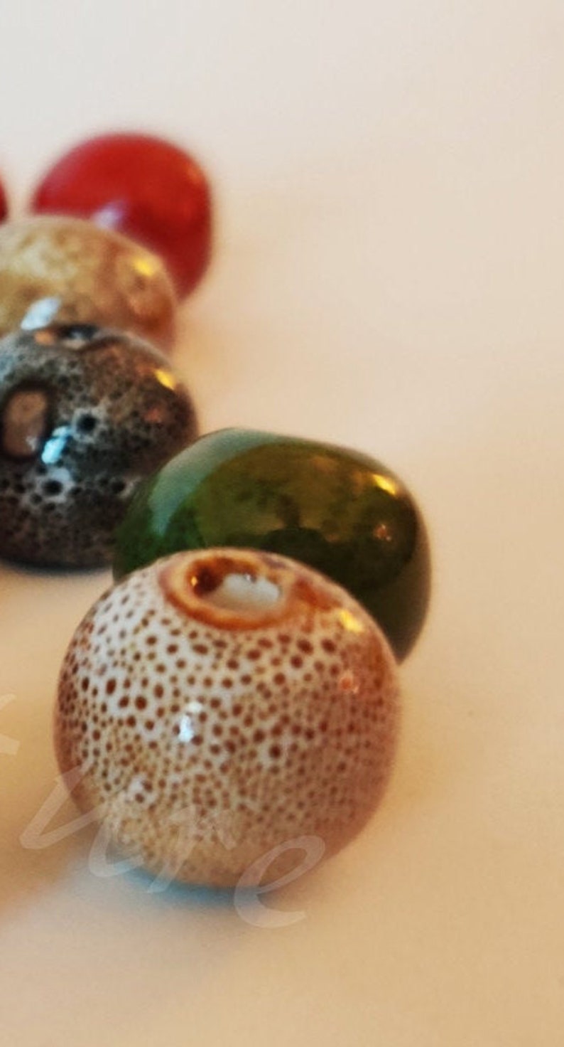 May include: A close-up of a collection of ceramic beads. The beads are various colors and have a speckled texture. The beads are round and have a hole in the center.