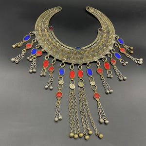 Può includere: Una collana d'argento e oro con perline di vetro rosse e blu e catene pendenti. La collana ha la forma di una mezzaluna ed è decorata con piccole punte di metallo.