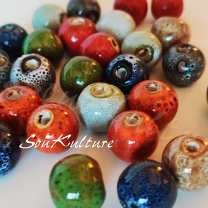 May include: A collection of ceramic beads in various colors, including green, blue, red, orange, and brown. The beads have a speckled or textured surface and are approximately 1 inch in diameter.