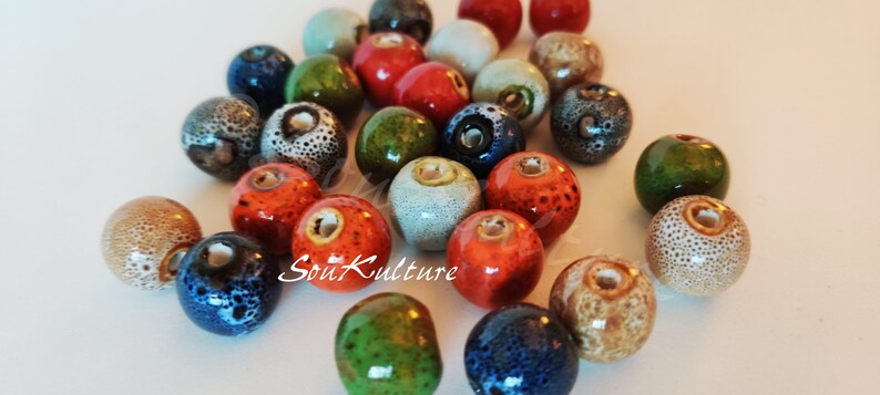 May include: A collection of ceramic beads in various colors, including green, blue, red, orange, and brown. The beads have a speckled or textured surface and are approximately 1 inch in diameter.
