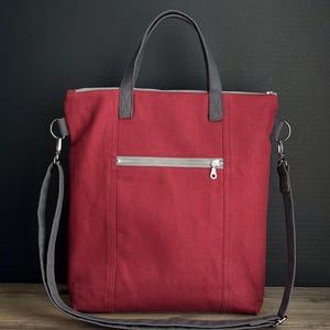 May include: A red tote bag with a gray zipper and a front pocket. The bag has gray handles and a detachable gray shoulder strap. The bag is made of a sturdy material and is suitable for everyday use.