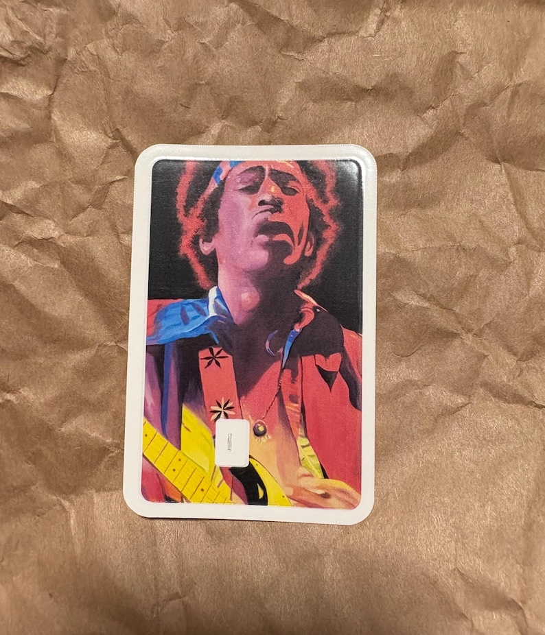 May include: Rectangular sticker featuring a vibrant illustration of a musician playing a yellow guitar. The image showcases the musician with a red jacket, blue accents, and a headband. The background is black.
