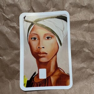 May include: A portrait of a woman with brown skin wearing a white head wrap with a green trim. The woman has brown eyes and is wearing a brown top. The artwork is on a white rectangular card.