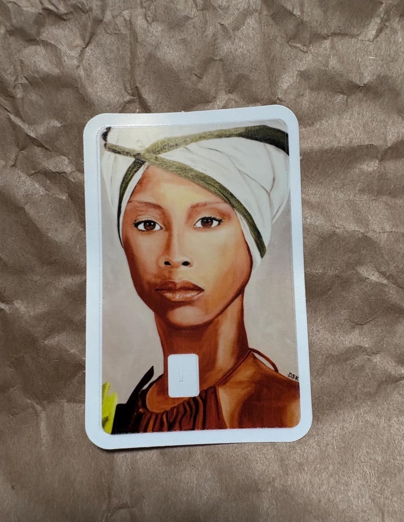 May include: A portrait of a woman with brown skin wearing a white head wrap with a green trim. The woman has brown eyes and is wearing a brown top. The artwork is on a white rectangular card.