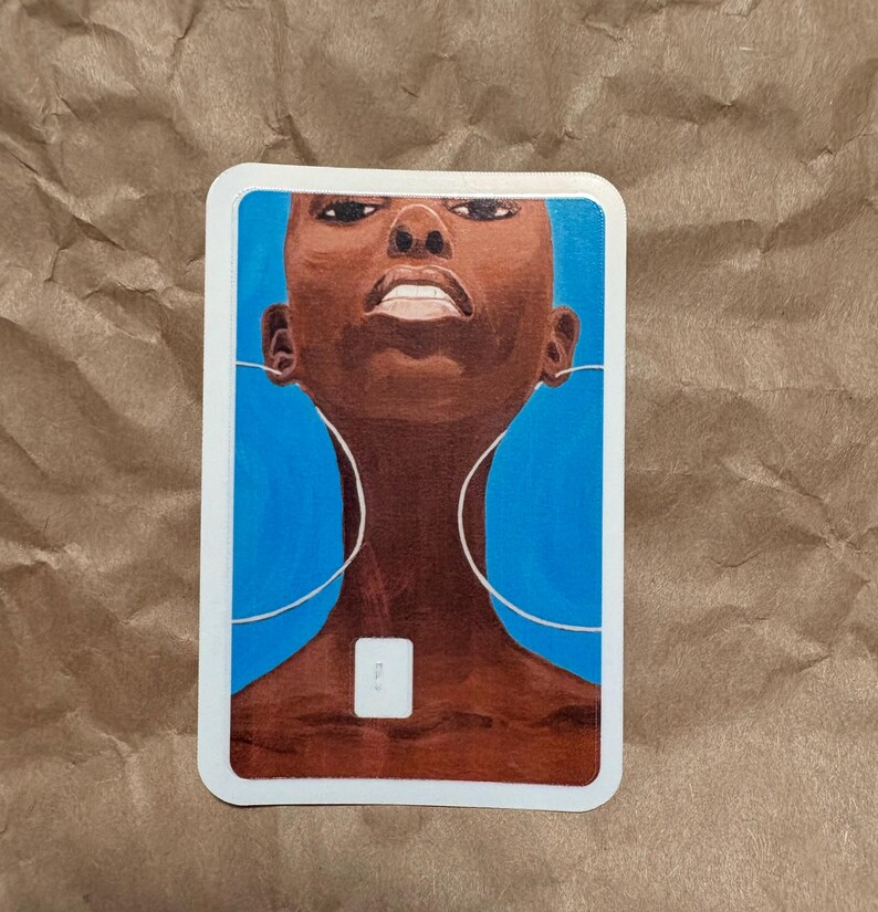 May include: A sticker featuring an illustration of a person with dark skin and a shaved head, set against a vibrant blue background. The artwork includes white lines suggesting headphones and a small white square. The sticker has a white border.
