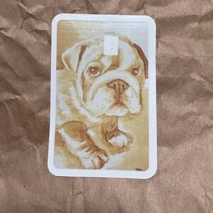 May include: A rectangular card featuring a watercolor painting of a bulldog puppy. The puppy has a light brown coat with darker brown markings and a sweet expression. The card has rounded corners and a white border.