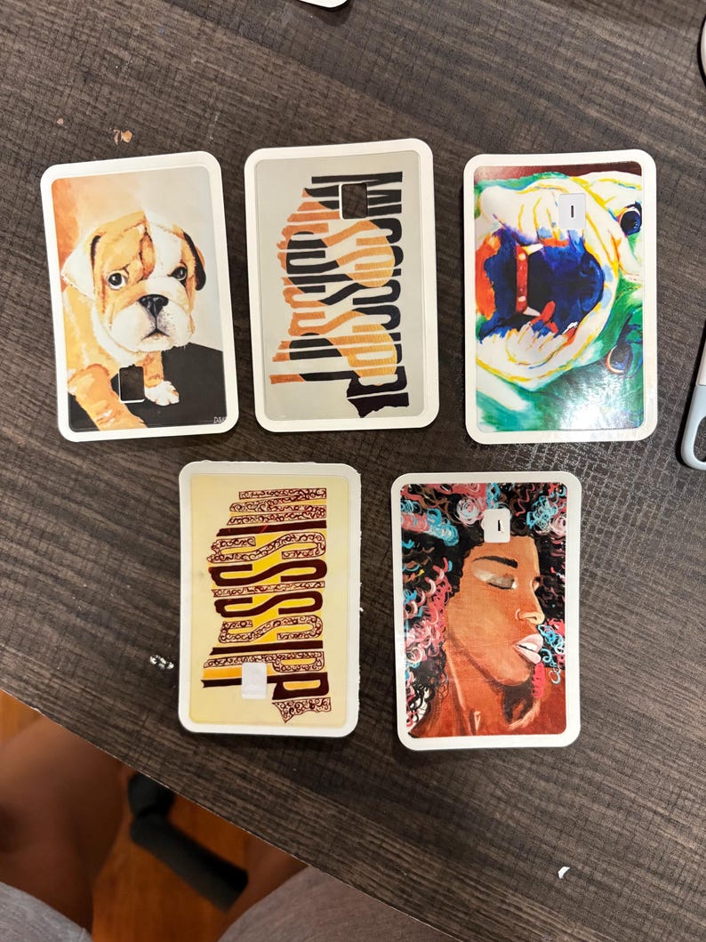 May include: Five rectangular decorative items with white borders. The images include a bulldog, abstract patterns, a colorful dog, a pattern with the word "Mississippi", and a portrait of a woman with colorful hair.