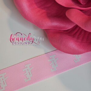 K&ouml;nnte beinhalten: Rosafarbenes Satinband mit wei&szlig;er Pr&auml;gung, auf dem "Kennedy Lynn Designs Crafting with you in mind" steht.
