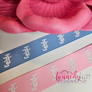 K&ouml;nnte beinhalten: Zwei Rollen Band mit einem sich wiederholenden wei&szlig;en Muster auf hellblauem und rosa Hintergrund. Das Band ist zum Basteln gedacht und tr&auml;gt den Text "Kennedy Lynn Designs Crafting with you in mind" auf dem rosa Band.