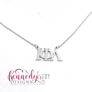May include: Silver necklace with a pendant featuring the Greek letters "ΚΦΛ".