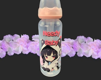 May include: A clear plastic baby bottle with a light pink screw-on cap and a translucent nipple cover. The bottle features a graphic of an anime-style character with dark hair and cat ears, accompanied by the red text Needy Baby printed above.