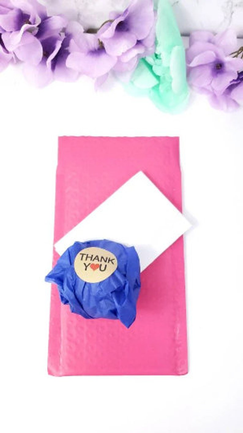 May include: A pink padded envelope with a white card and a blue tissue paper wrapped package with a brown sticker that says "THANK YOU" with a red heart.