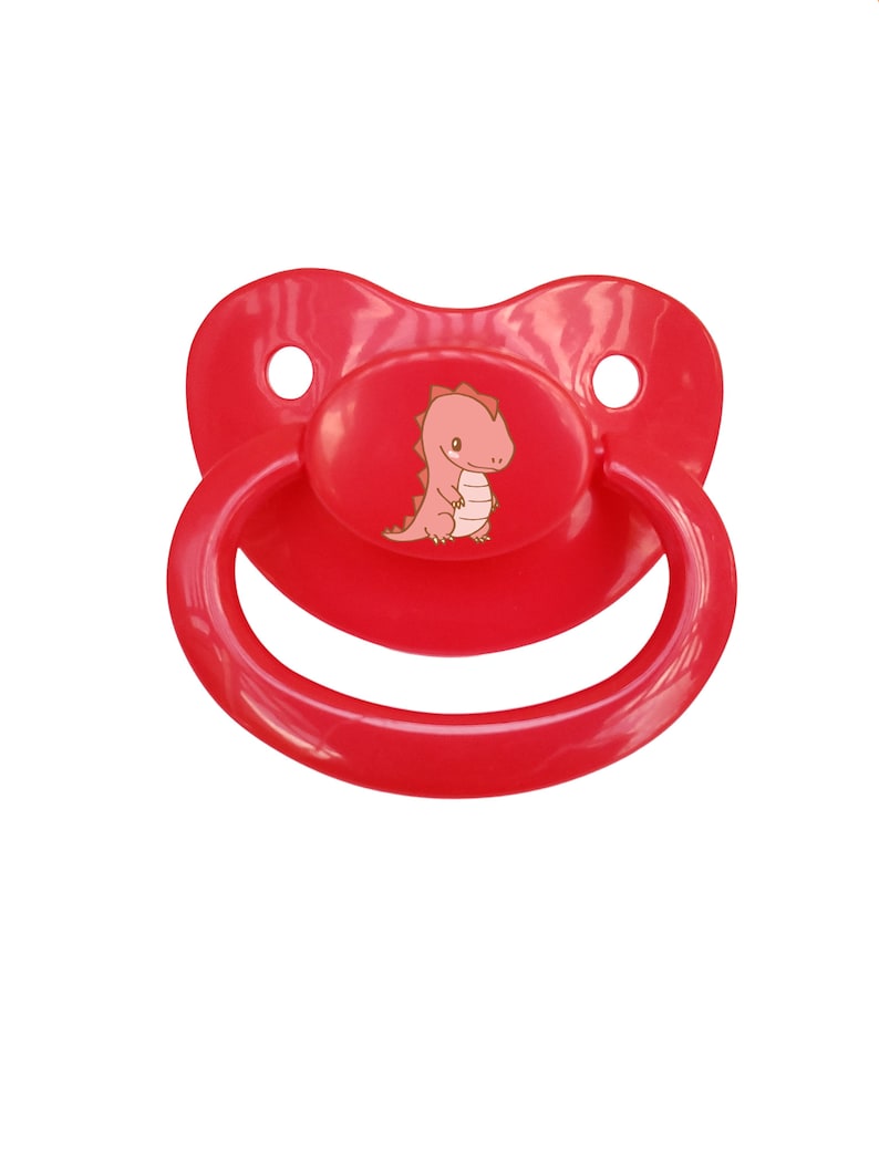 May include: A red pacifier with a cartoon dinosaur design. The dinosaur is pink and has a brown outline.