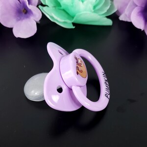 May include: A purple pacifier with a sloth design and the word "PUMPKIN" printed on the side.