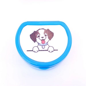 May include: A blue plastic container with a white lid featuring a cartoon dog with brown ears and a red tongue. The dog is looking at the viewer and has a white collar.
