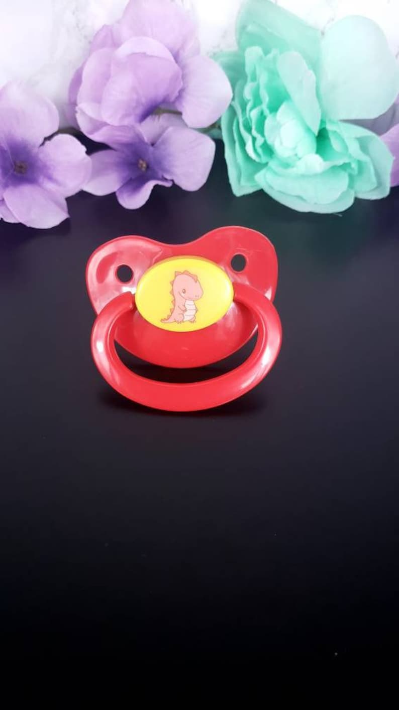 May include: Red pacifier with a yellow and pink dinosaur design.