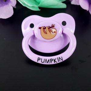 May include: Purple pacifier with a sloth design and the word "PUMPKIN" printed on the bottom.