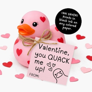 以下が含まれることがあります： 赤いハートで飾られたピンク色のラバーダックとオレンジ色のくちばし。紐で結ばれたピンク色のカードには、アヒルのイラストとともに「Valentine, you QUACK me up!」と書かれています。赤とピンクのハート型の切り抜きが散らばっています。