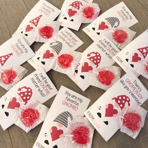 May include: A set of Valentine's Day cards featuring gnomes and hearts. The cards are decorated with red and white polka dots and have a variety of messages, including "You are my favorite gnome!" and "I will be your friend gnome matter what!" Each card includes a small red lollipop.