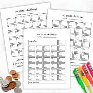 May include: Three white paper sheets with a black grid layout for a "NO SPEND challenge" are displayed. The sheets include spaces for tracking spending and a section to write the reason for the challenge. Coloured pens and coins are also visible.
