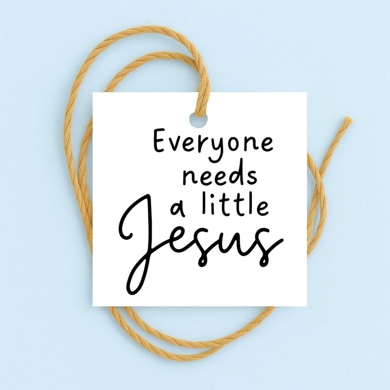 May include: A white square tag with the text "Everyone needs a little Jesus" in black script. The tag is suspended by a tan twine loop against a light blue background.