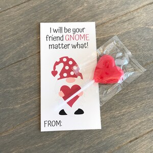 May include: A Valentine's Day card with a gnome holding a heart. The card reads "I will be your friend GNOME matter what!" and has a space for "FROM:". A red heart-shaped lollipop is included.