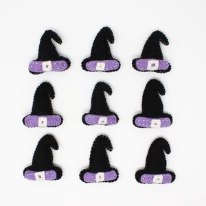 May include: Nine felt witch hats with purple trim and a white button. The hats are arranged in three rows of three.